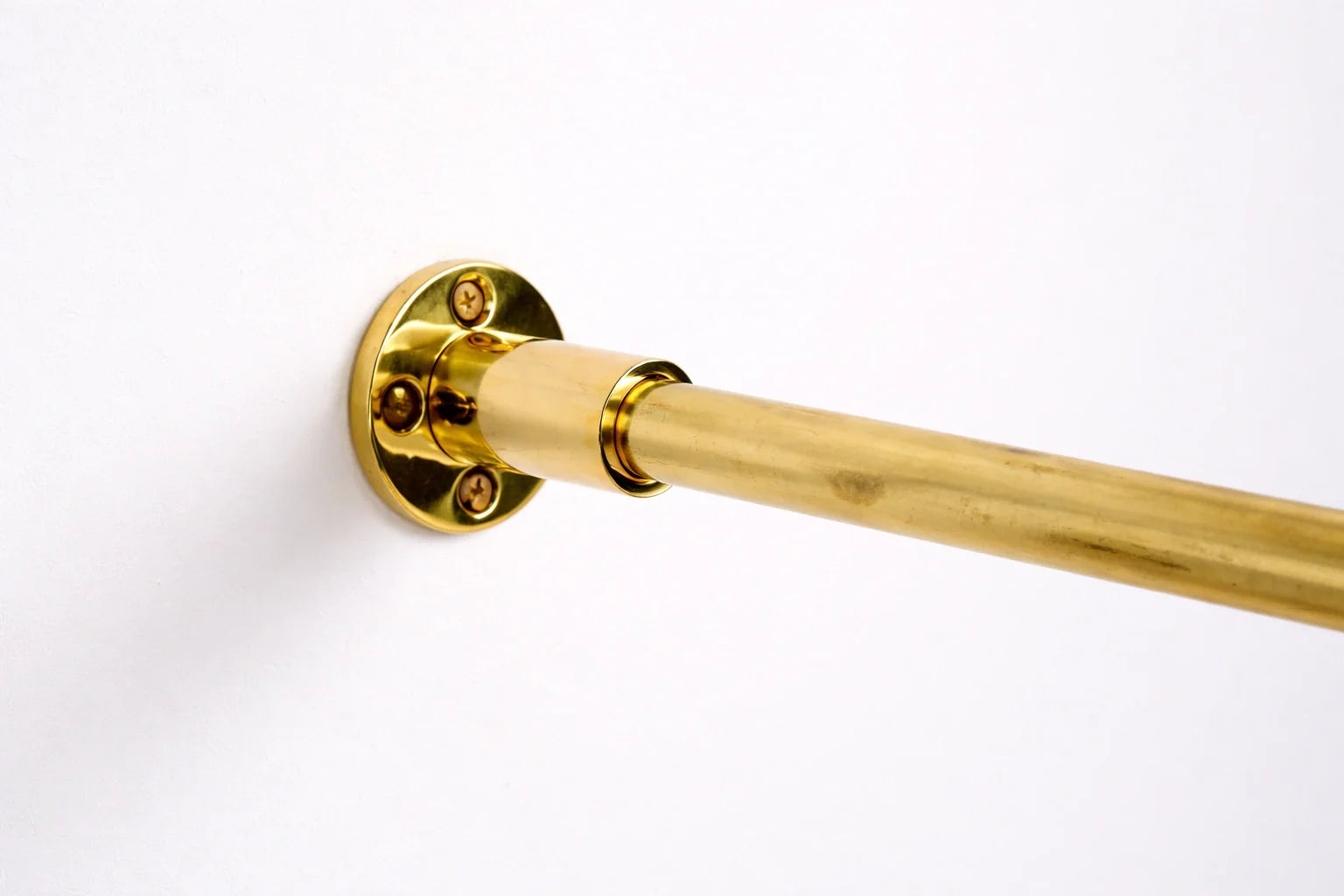 Close-up of a polished brass curtain rod mounted on a matte white textured wall with soft natural lighting