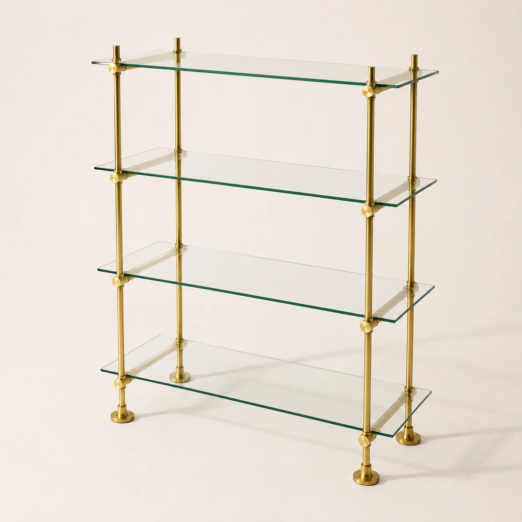 A 4-tier glass shelf bookcase with a polished brass frame, featuring clear glass shelves and round brass finials at the joints and feet, set against a plain off-white background.