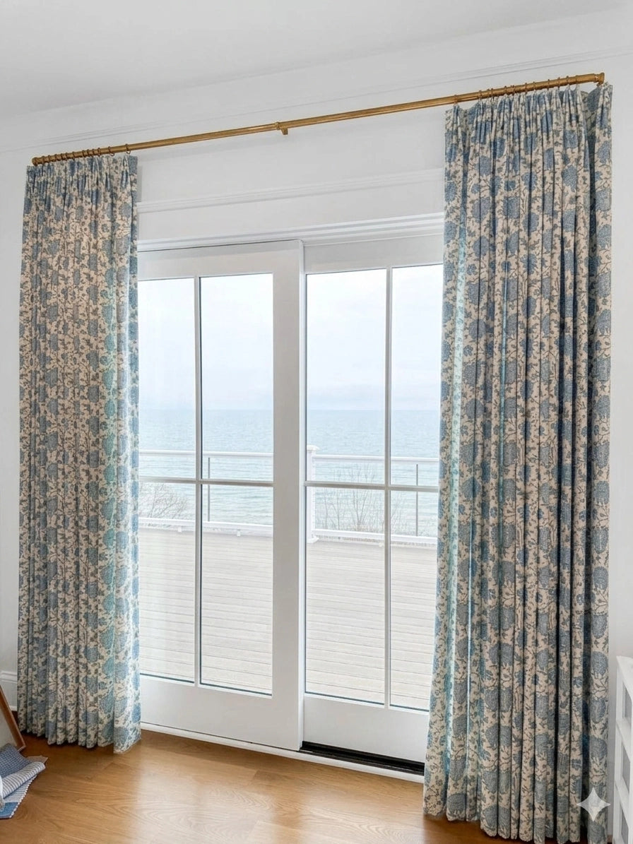 Patterned curtains on a rod in front of a glass door with a view of a balcony.