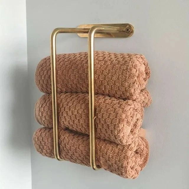 Wall-mounted brass towel rack holding three neatly rolled brown textured towels