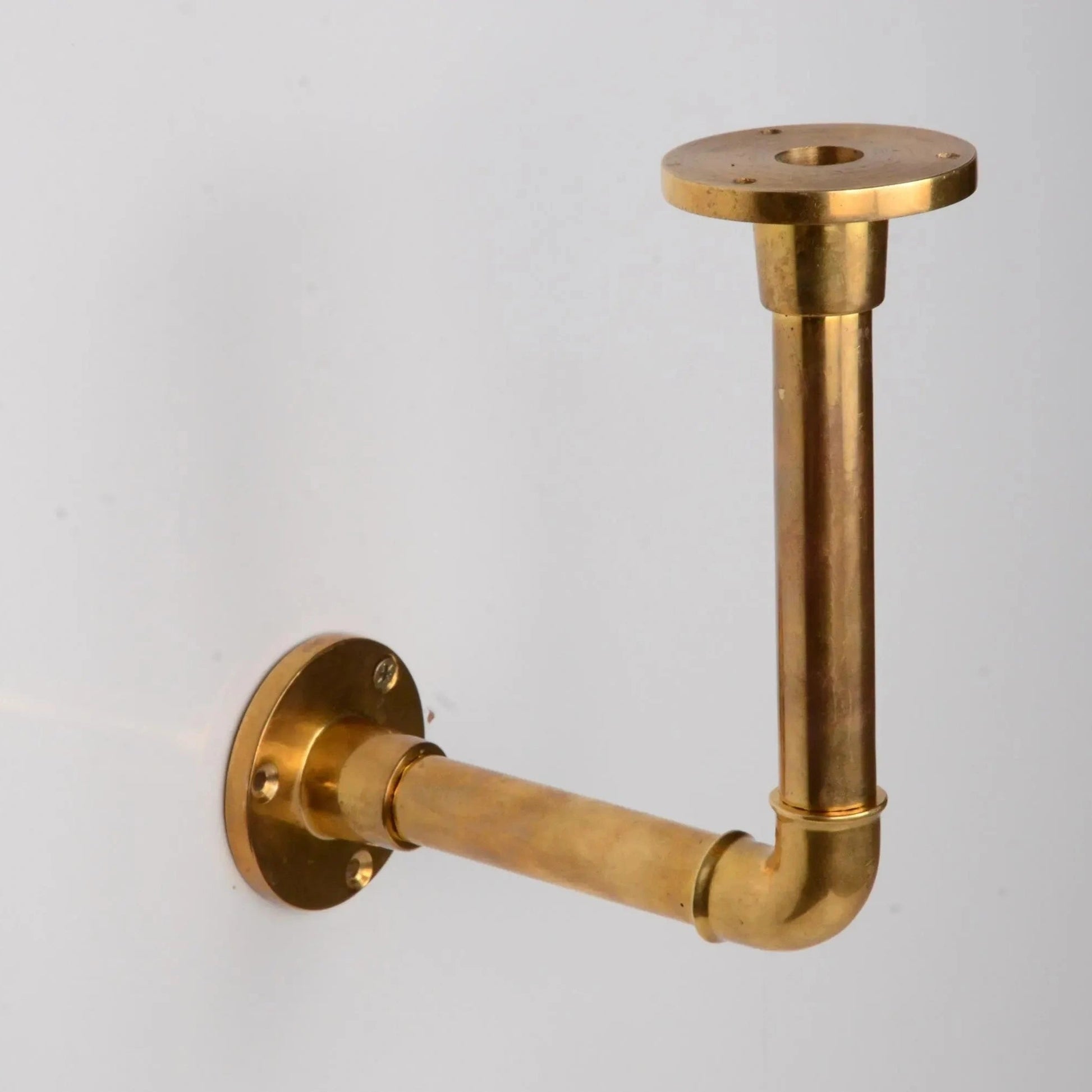Solid unlacquered brass pipe bracket mounted on a white wall, designed for supporting floating shelves. atlas finest