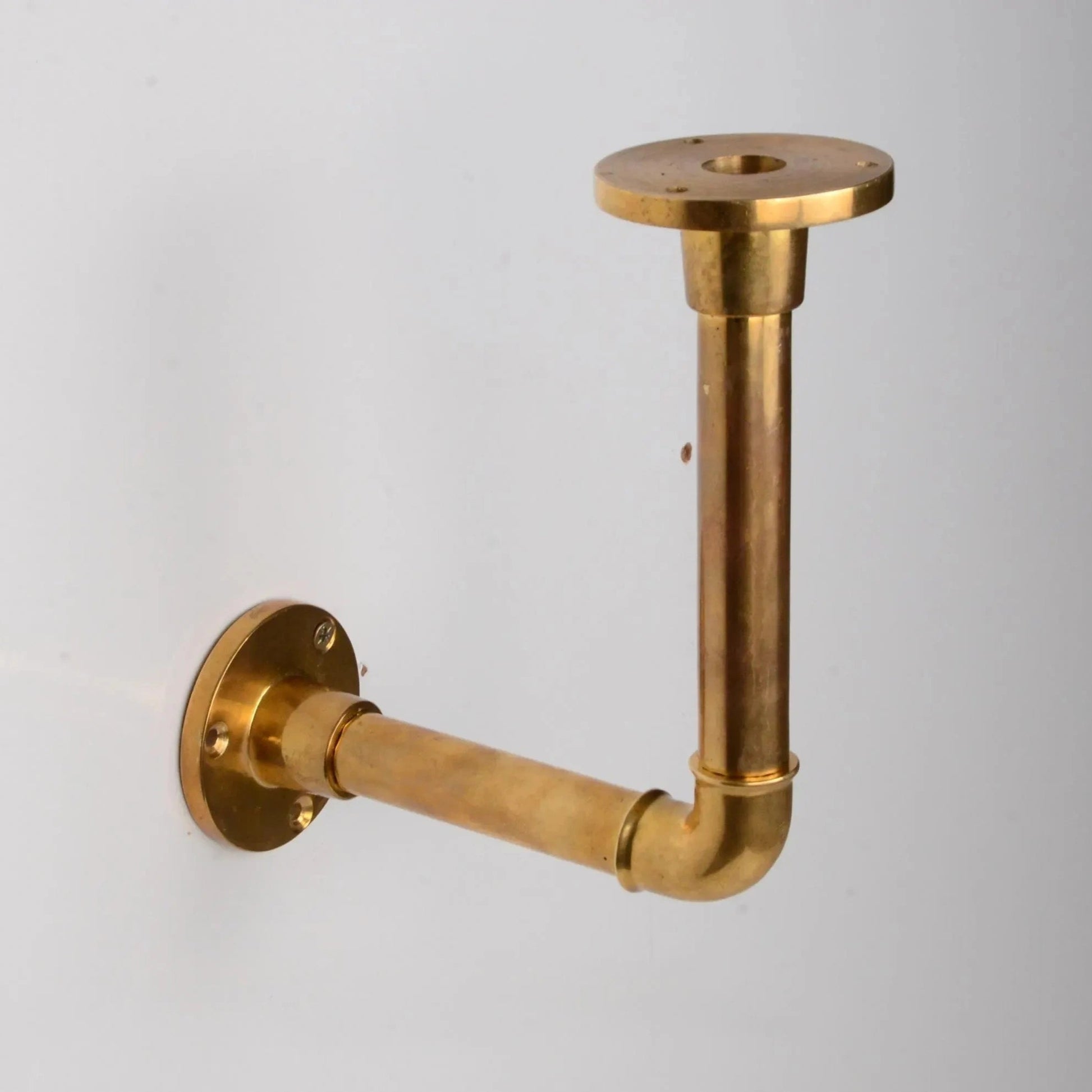 Solid unlacquered brass pipe bracket mounted on a white wall, designed for supporting floating shelves. atlas finest
