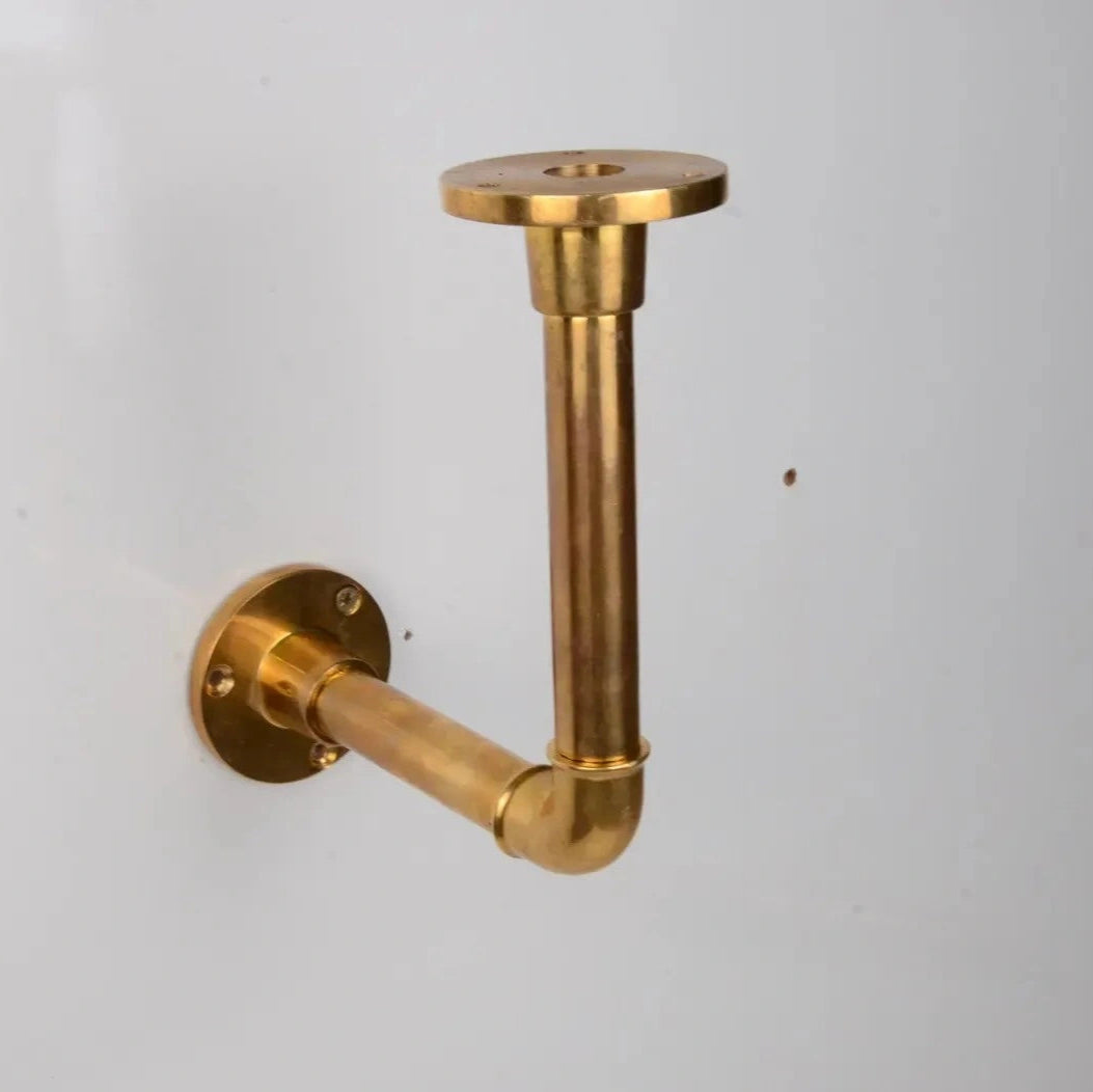 Solid unlacquered brass pipe bracket mounted on a white wall, designed for supporting floating shelves. atlas finest