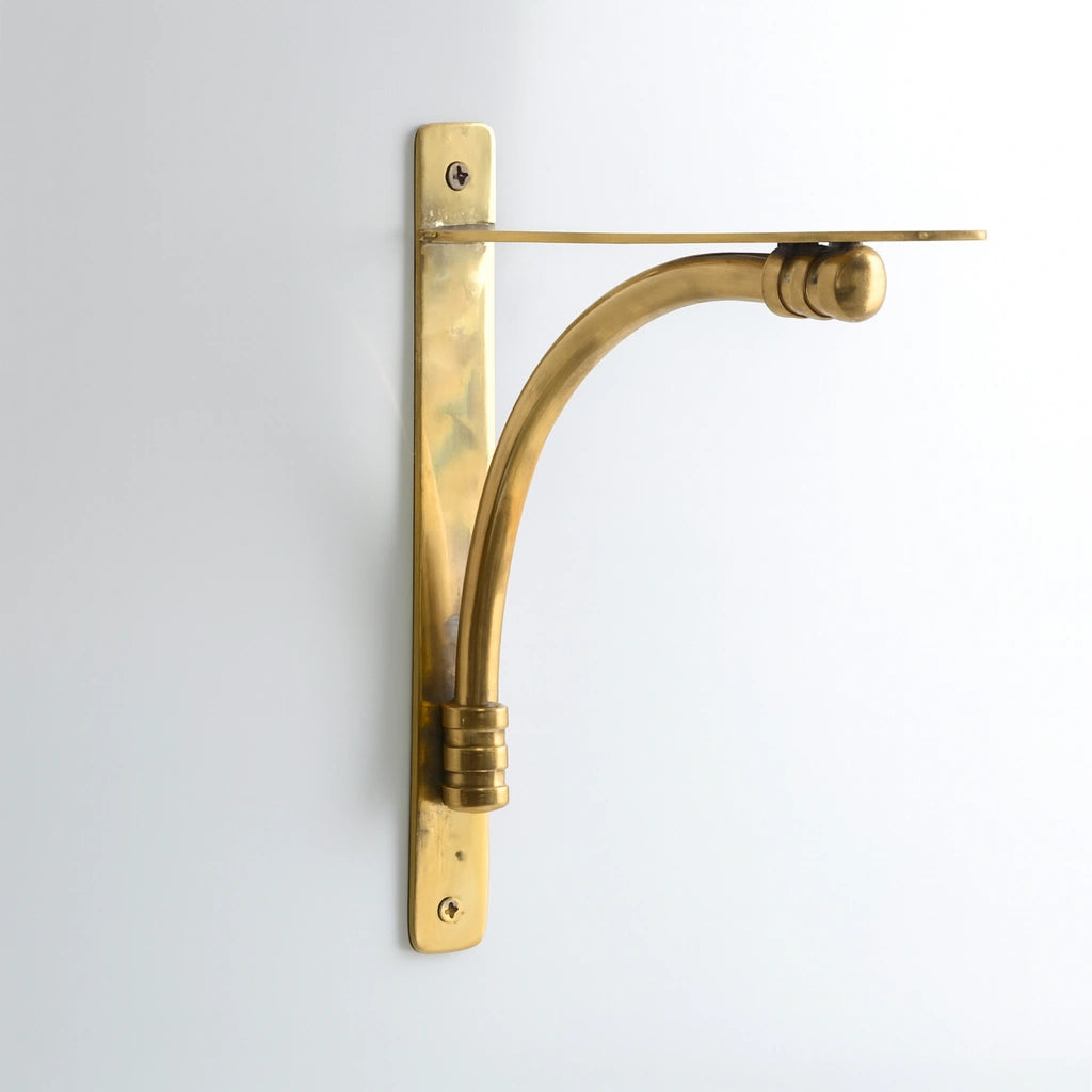 Polished solid unlacquered brass shelf bracket mounted on a clean white wall, minimalistic and elegant design.