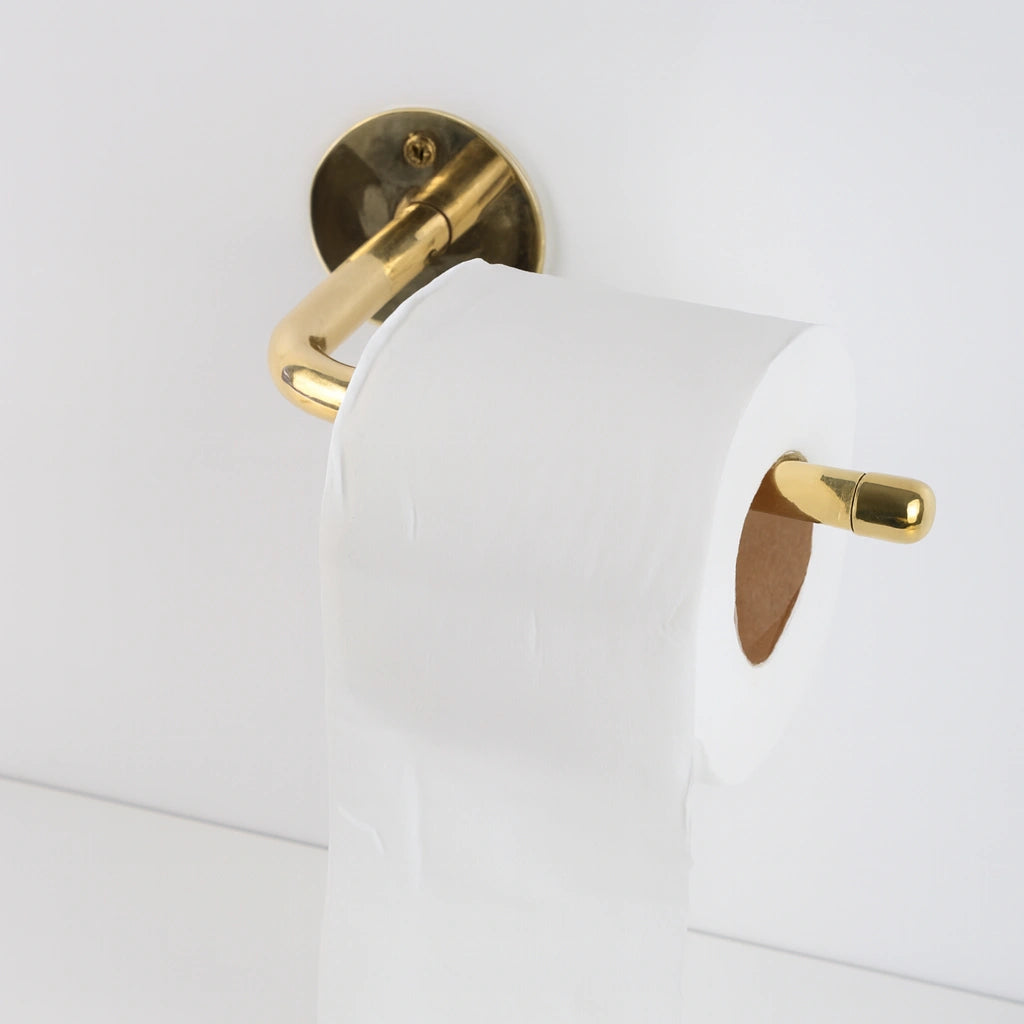 Alt text: A white toilet paper roll on a polished unlacquered brass holder against a clean white wall.
