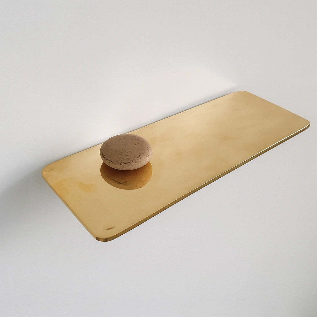 Minimalist long unlacquered brass floating shelf with smooth polished finish and decorative stone accent on white wall