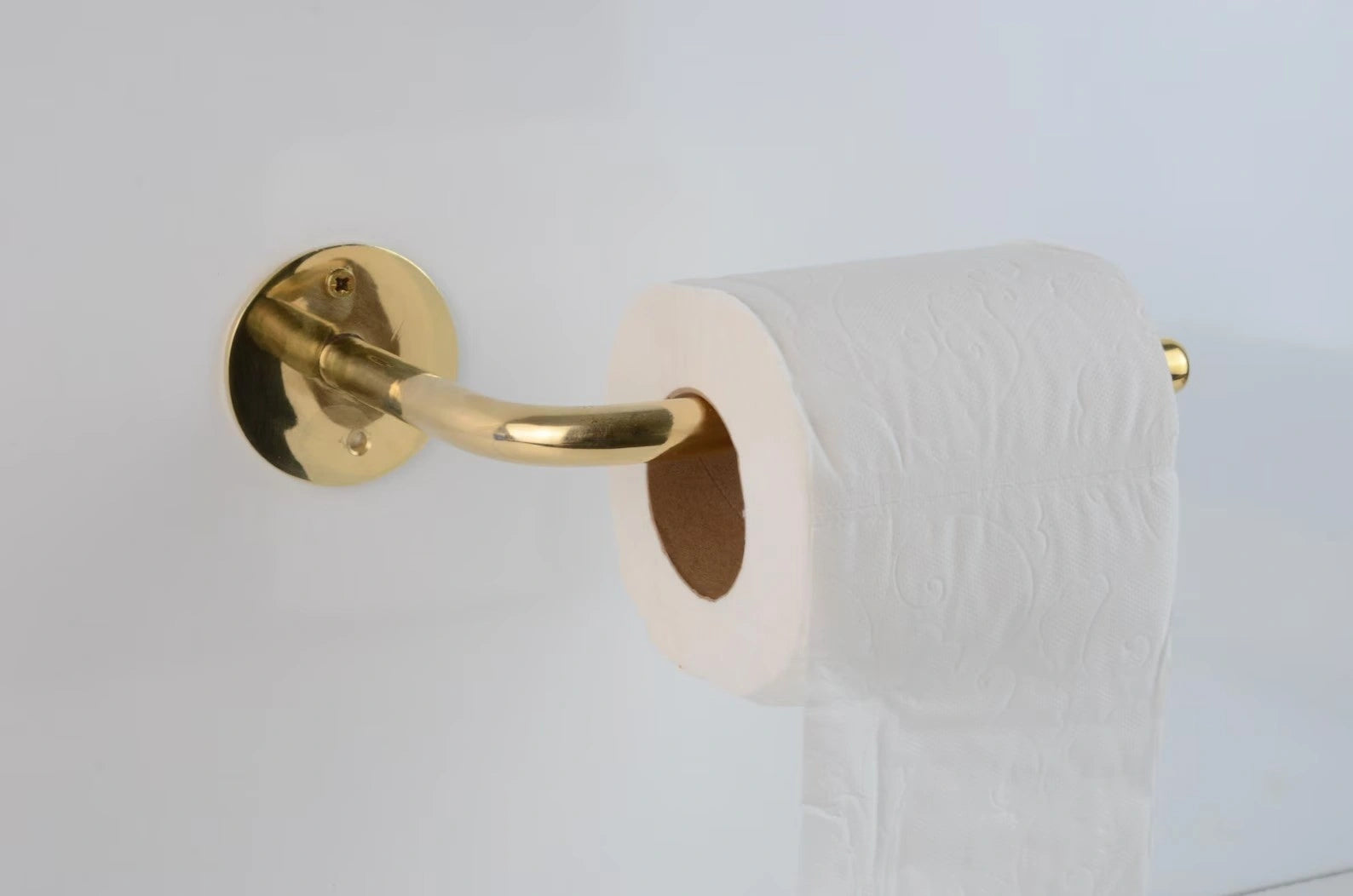 Elegant unlacquered brass toilet paper holder with a white tissue roll on a clean white wall