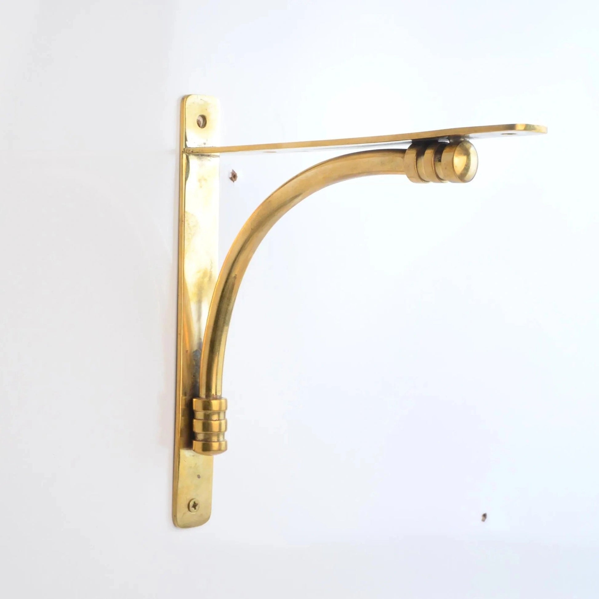 Solid unlacquered brass shelf bracket mounted on a white wall with a minimalist design.